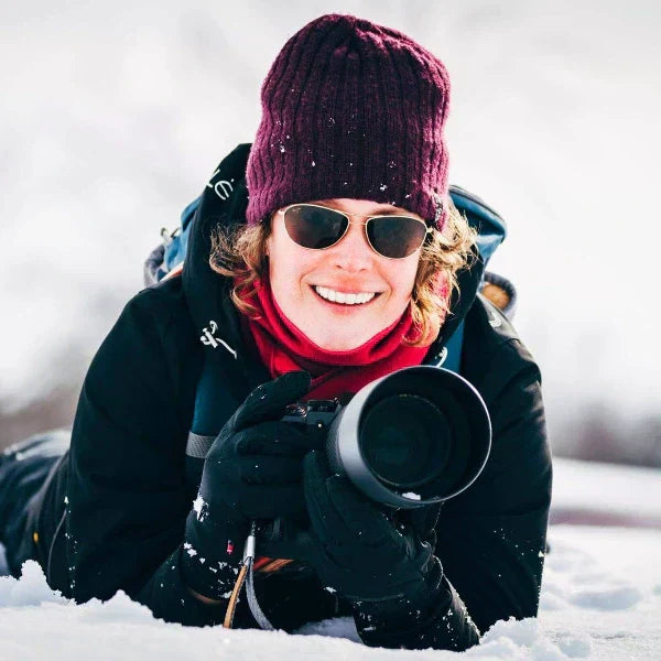 Nature photographer Jinny Montpetit lying in snow with camera, capturing wildlife and landscapes for Feathered Stories